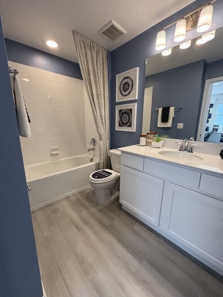 A stylish bathroom featuring a blue accent wall, a classic white vanity, and a tiled bathtub in Eden at Crossprairie by M/I Homes (St. Cloud, FL).