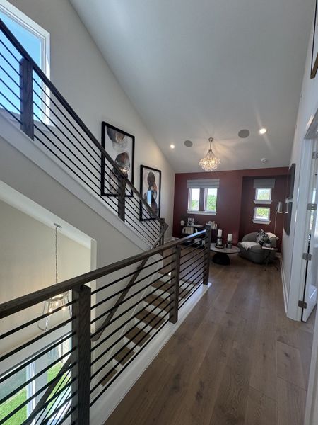 A modern hallway with wood flooring, chic railings, a cozy seating nook, and stylish wall art, illuminated by natural light.