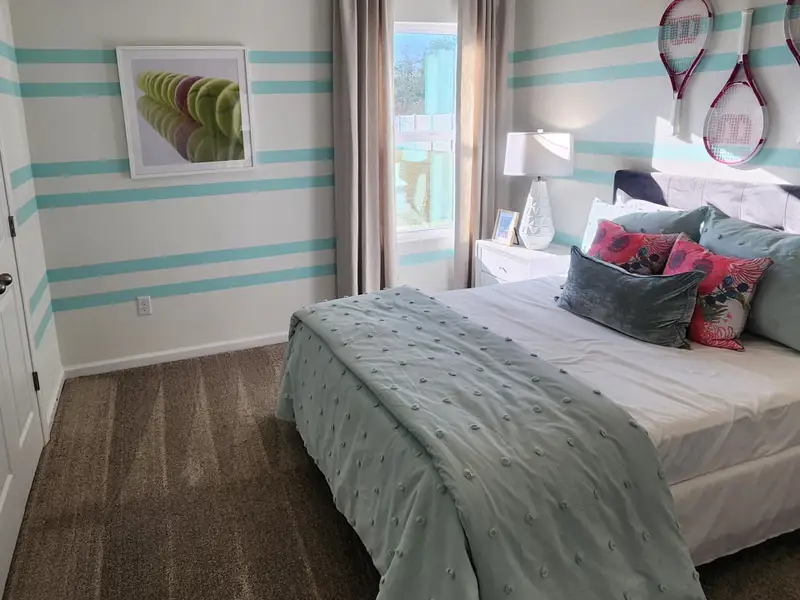 A fun tennis-themed bedroom with striped accent walls, sporty décor, and cozy bedding in Panther Creek by KB Home (Jacksonville, FL).