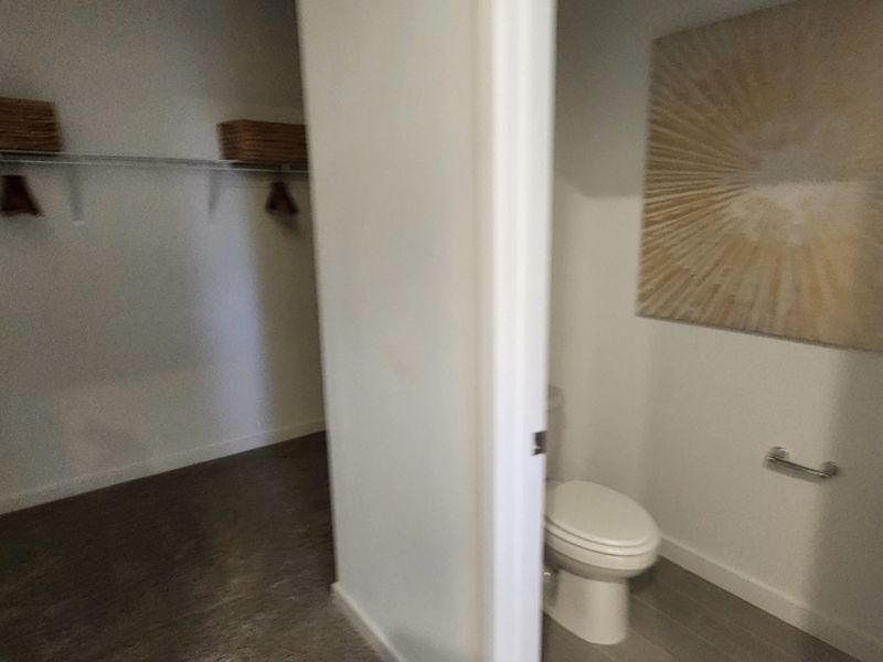 A spacious walk-in closet with open shelving next to a small, modern bathroom featuring minimalist decor.