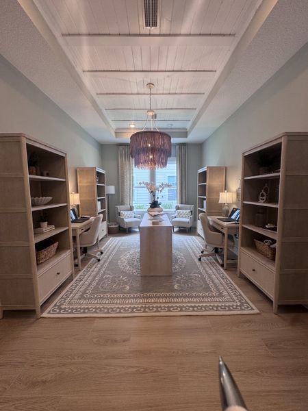 A cozy office space featuring built-in shelving, elegant wood flooring, and a chic chandelier.