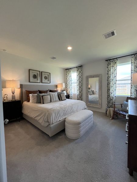 A cozy bedroom with a plush bed, patterned curtains, elegant lamps, and a large decorative mirror.