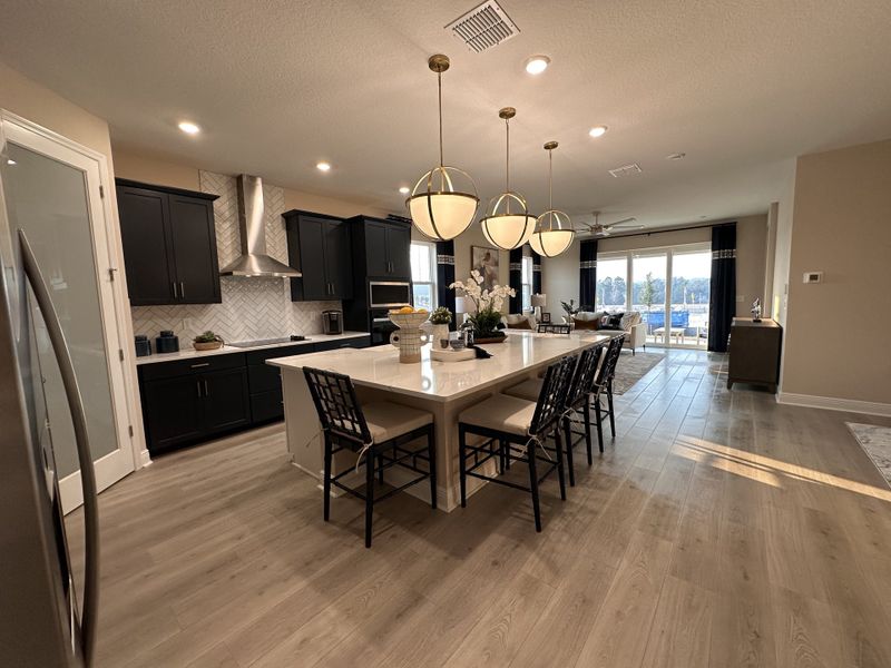 A beautifully designed kitchen with dark cabinetry, gold lighting, and an oversized island in Crossroads at Kelly Park by Dream Finders Homes (Apopka, FL).