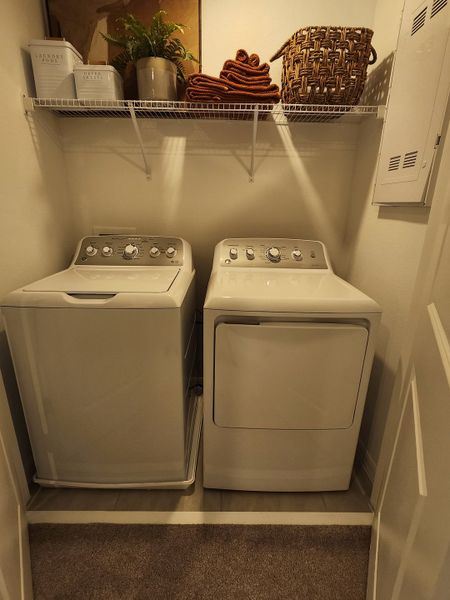 A cozy laundry nook with a modern washer and dryer, overhead shelving, and stylish baskets for storage.