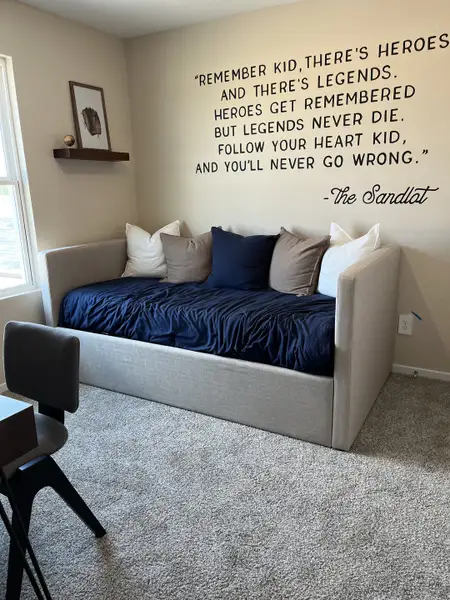 Cozy room with a daybed, motivational wall quote, and a small shelf, perfect for relaxation or study.