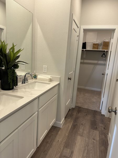 A modern bathroom with dual sinks, wooden flooring, sleek cabinetry, and an adjoining walk-in closet.