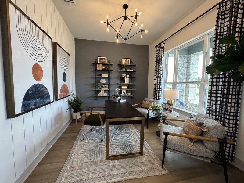 A modern home office with geometric art, a sleek desk, cozy chairs, and stylish shelves.