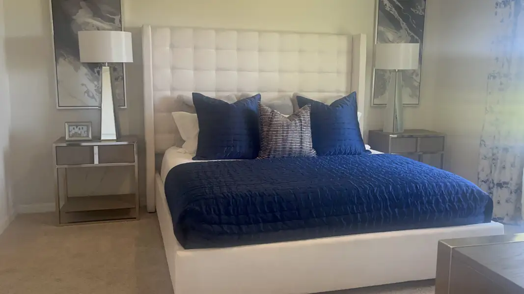 A cozy bedroom with a plush white headboard, deep blue bedding, modern lamps, and elegant side tables.