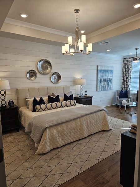 A cozy bedroom featuring a textured accent wall, elegant chandelier, plush bedding, and chic decor.