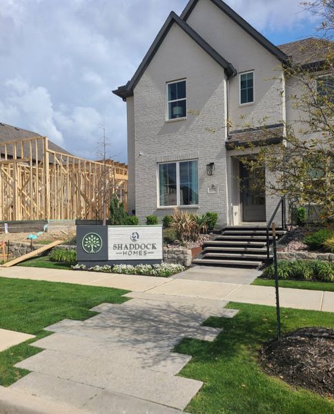 A charming white brick home with manicured landscaping at The Grove Frisco - 40' Lots by Shaddock Homes (Frisco, TX).