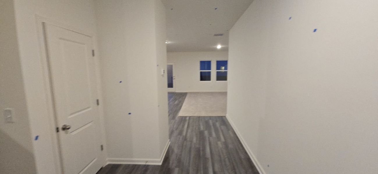 A modern hallway with sleek flooring, neutral walls, and bright lighting leading to an open living area.