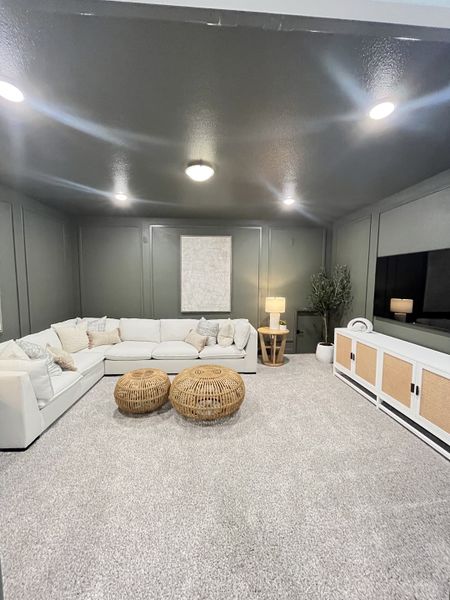 A cozy living room features a plush sectional, woven ottomans, and sleek TV console with soft carpeted flooring.