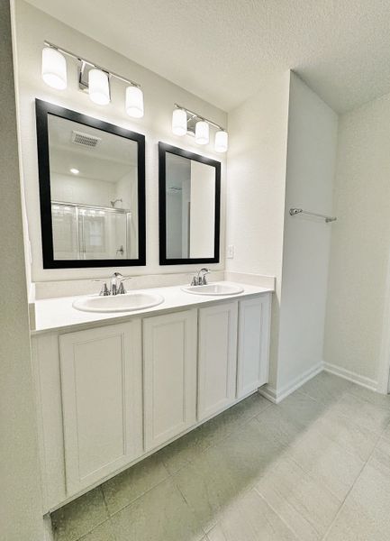 A bright bathroom with dual sinks, sleek black-framed mirrors, and modern lighting fixtures.