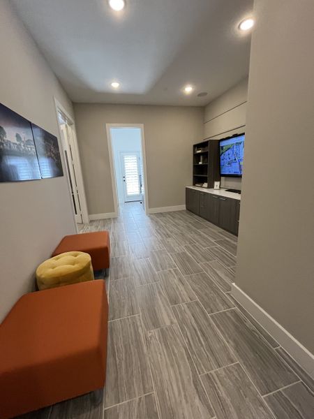 A contemporary hallway with sleek grey tiles, a built-in entertainment unit, and cozy orange seating.