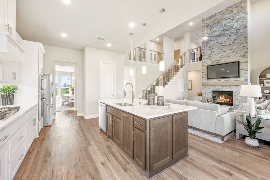 Open-concept kitchen with large island flowing into living room with stone fireplace and two-story ceiling Open-concept kitchen with large island flowing into living room with stone fireplace and two-story ceiling