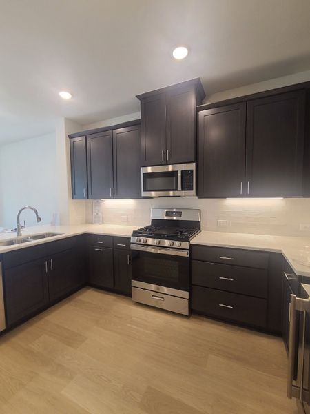 A modern kitchen featuring dark cabinets, stainless steel appliances, and sleek light countertops.