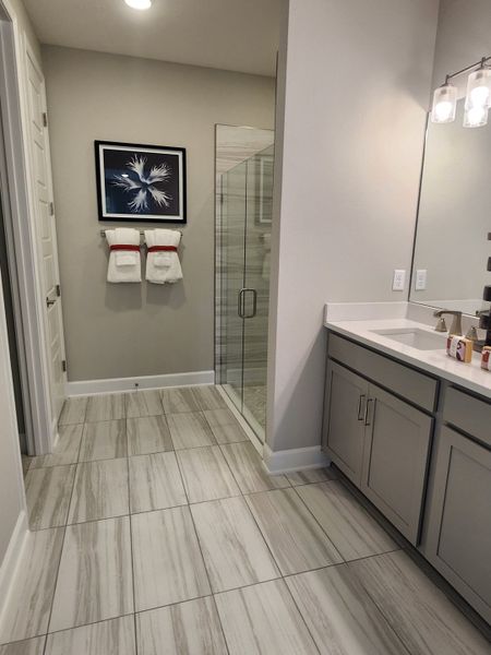A modern bathroom featuring a glass shower, elegant tile flooring, sleek cabinetry, and artistic wall decor.