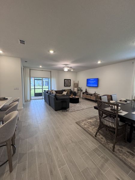 A modern living area with sleek gray flooring, cozy seating, and a large dining table adjacent to a windowed patio door.