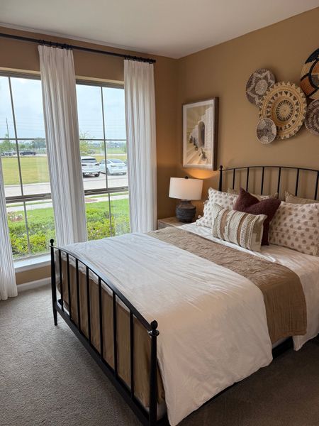 Cozy bedroom featuring warm earth tones, large windows with sheer curtains, and decorative wall art for a relaxing ambiance.