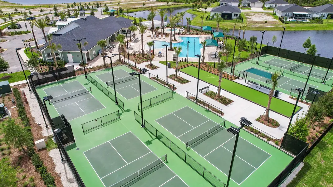 Aerial view of community pickleball courts with pool, clubhouse, and lake in background