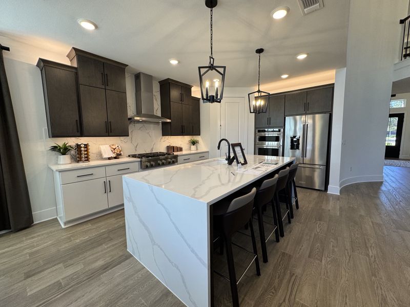 A modern kitchen with sleek dark cabinets, marble countertops, and elegant pendant lighting.