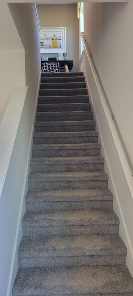 A modern staircase with plush gray carpeting and sleek handrails, leading to a cozy, art-adorned landing area.