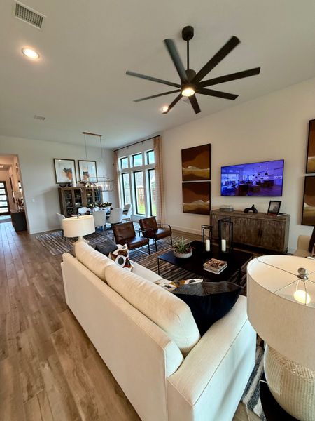 A modern living room featuring wood floors, a ceiling fan, chic lighting, and cozy seating with stylish decor.