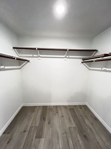 A spacious walk-in closet with sleek hardwood floors and ample shelving for organized storage.