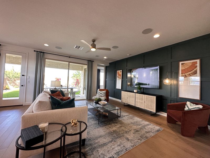 A modern living room with a beige sofa, dark accent wall, and sliding glass doors opening to a lush backyard.
