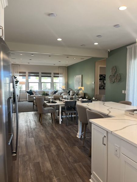 An open-concept dining area with elegant decor, wood flooring, and soft green walls, leading into a cozy living space.