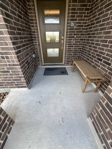 A welcoming brick entryway with a modern door and rustic bench in Oakwood Trails by KB Home (Tomball, TX).