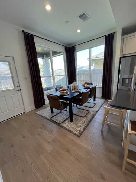 A modern dining area with wooden floors, large windows, and dark curtains, creating a cozy and inviting space.