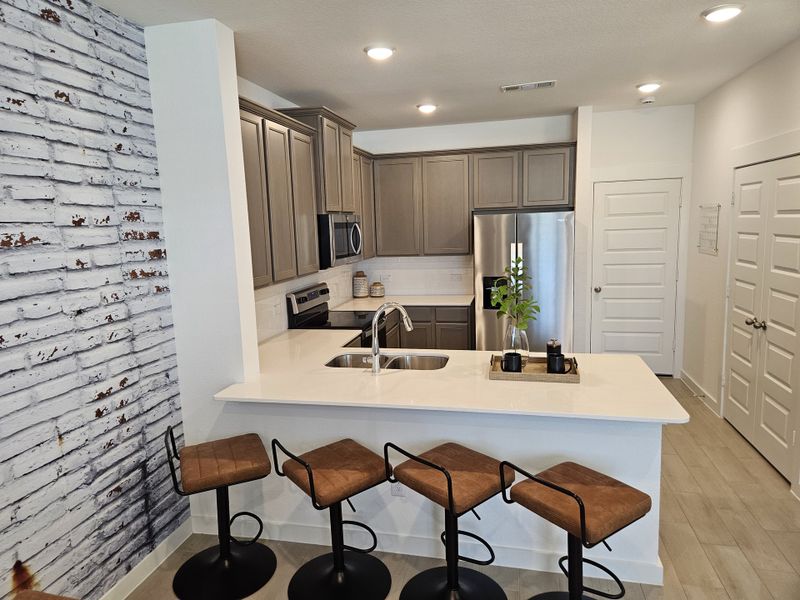 A modern kitchen with a white brick accent wall, sleek cabinets, and a cozy breakfast bar with stylish brown stools. A modern kitchen with a white brick accent wall, sleek cabinets, and a cozy breakfast bar with stylish brown stools.