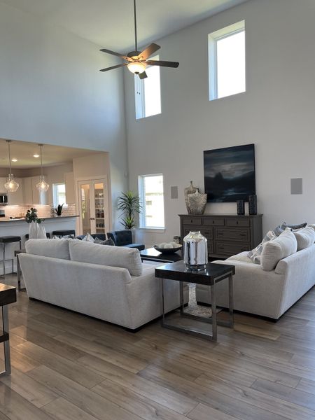 An inviting living room with high ceilings, light wood floors, plush sofas, and a modern ceiling fan for a cozy ambiance.