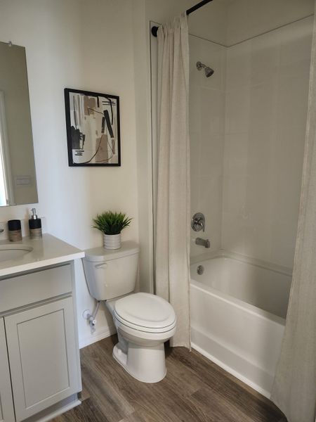 A modern bathroom with a sleek white bathtub, light wood flooring, and minimalistic décor.