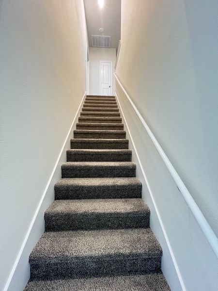 A carpeted staircase with neutral walls leads to a bright upper floor, showcasing modern, minimalist elegance.