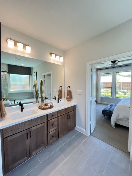 A modern bathroom with dual sinks, wooden vanity, and sleek lighting leading to a cozy bedroom bathed in natural light.