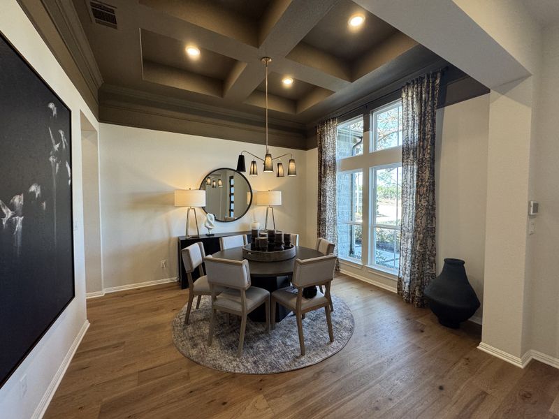 A sophisticated dining room featuring a coffered ceiling, round table, elegant drapes, and modern art.