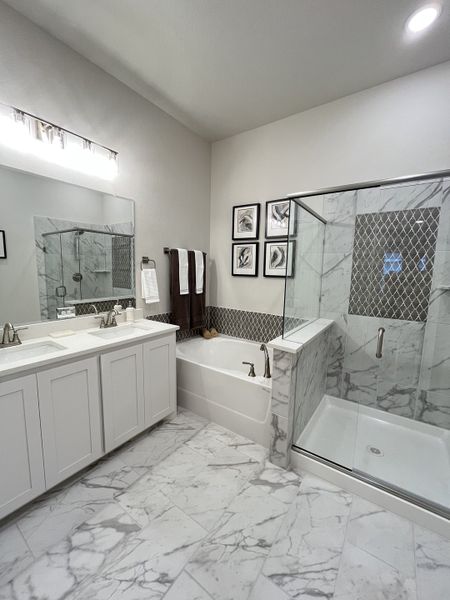 A modern bathroom with marble tile, a glass shower, dual sinks, and elegant decor.