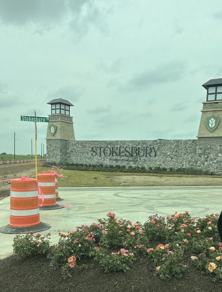 Stokesbury entrance with a stone wall and blooming flowers by Centex in Waller, TX.