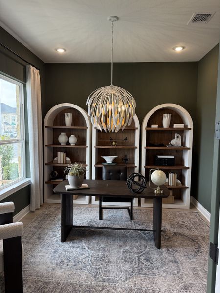 A sophisticated home office with built-in shelves, modern chandelier, and large window.
