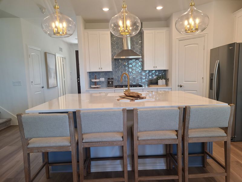A chic kitchen with a large white island, glass pendant lights, and elegant wood stools.