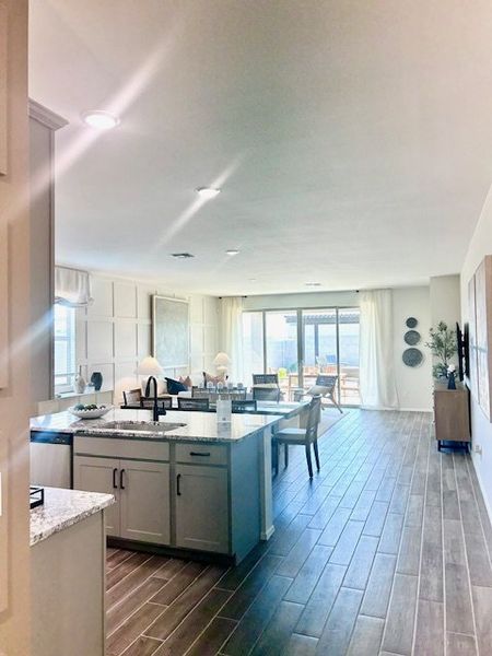 A spacious kitchen with a central island, sleek countertops, and open layout leading to a dining area and sunlit patio.