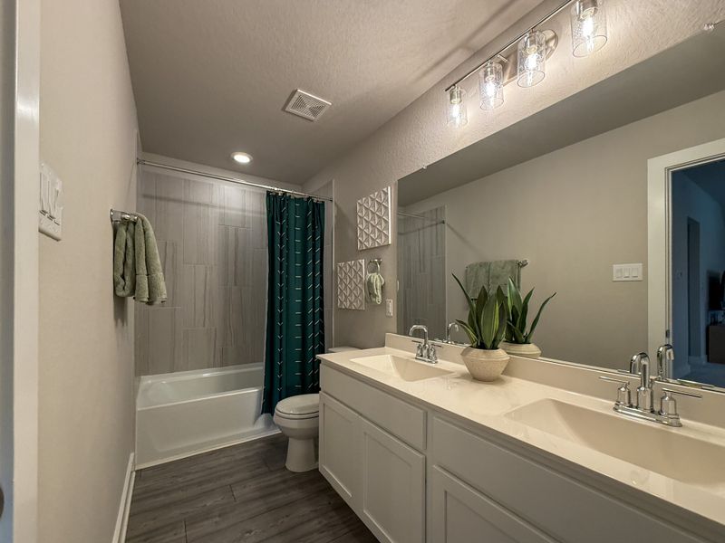 A modern bathroom featuring a large mirror, dual sinks, and a chic wooden floor with green accents.