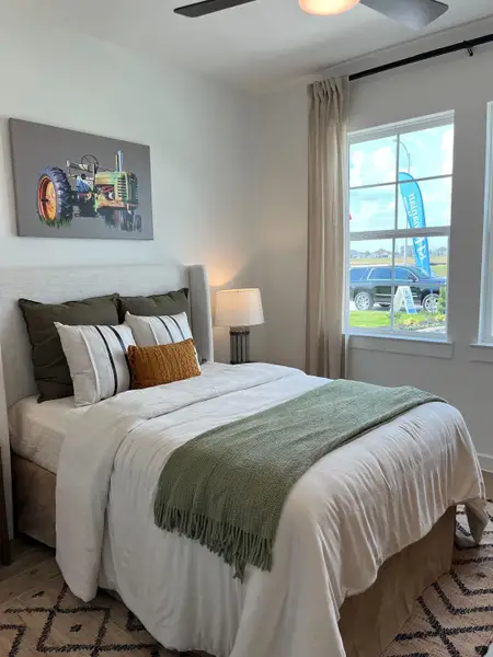 Cozy bedroom featuring a plush bed with mixed pillows, a green throw, modern lamp, and chic tractor artwork.