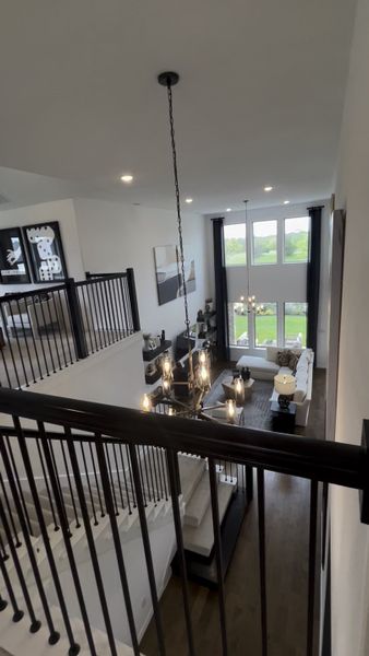 An elegant living room with high ceilings, large windows, and a chic chandelier, overlooking a lush green view.