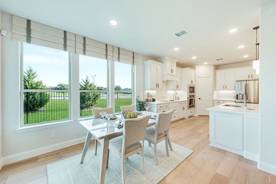 Open dining area and kitchen with white cabinets, hardwood floors, and large windows overlooking a backyard Open dining area and kitchen with white cabinets, hardwood floors, and large windows overlooking a backyard