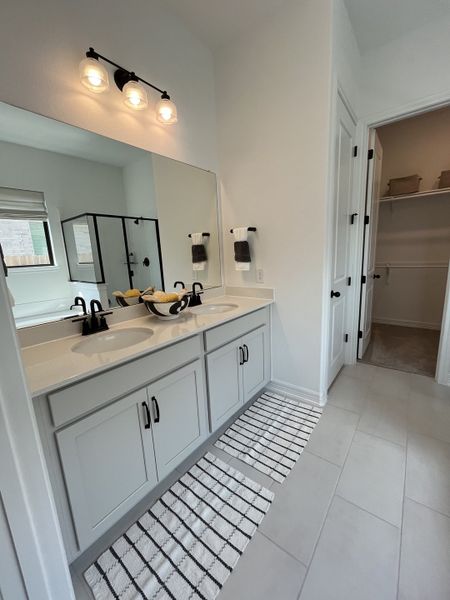 A modern bathroom featuring dual sinks, sleek cabinetry, and elegant lighting with a walk-in shower and closet access. A modern bathroom featuring dual sinks, sleek cabinetry, and elegant lighting with a walk-in shower and closet access.