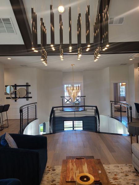 A modern living space with sleek chandeliers, a curved railing, and stylish wood flooring creates an inviting ambiance.