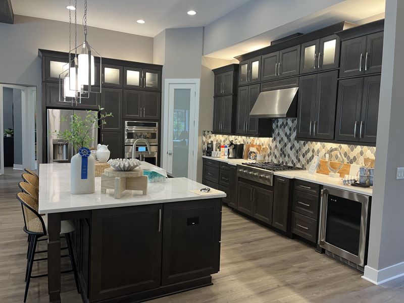 A modern kitchen featuring dark wood cabinets, stainless appliances, a spacious island, and sleek pendant lighting.